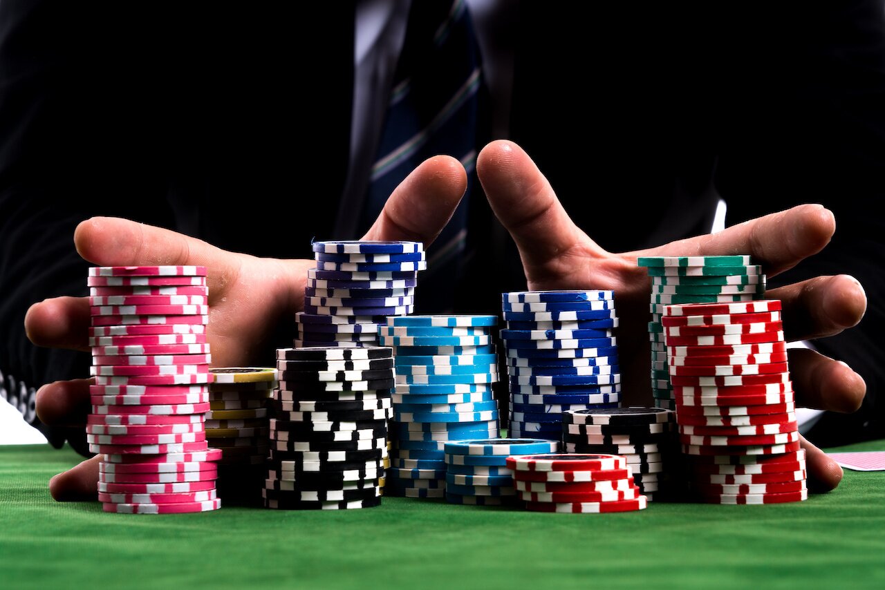 Gambler man hands pushing large stack of colored poker chips across gaming table for betting