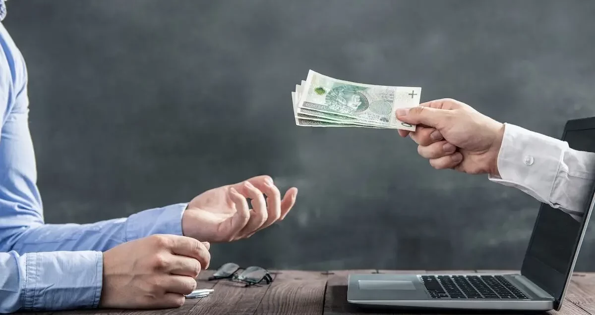 hand through a laptop giving a man money