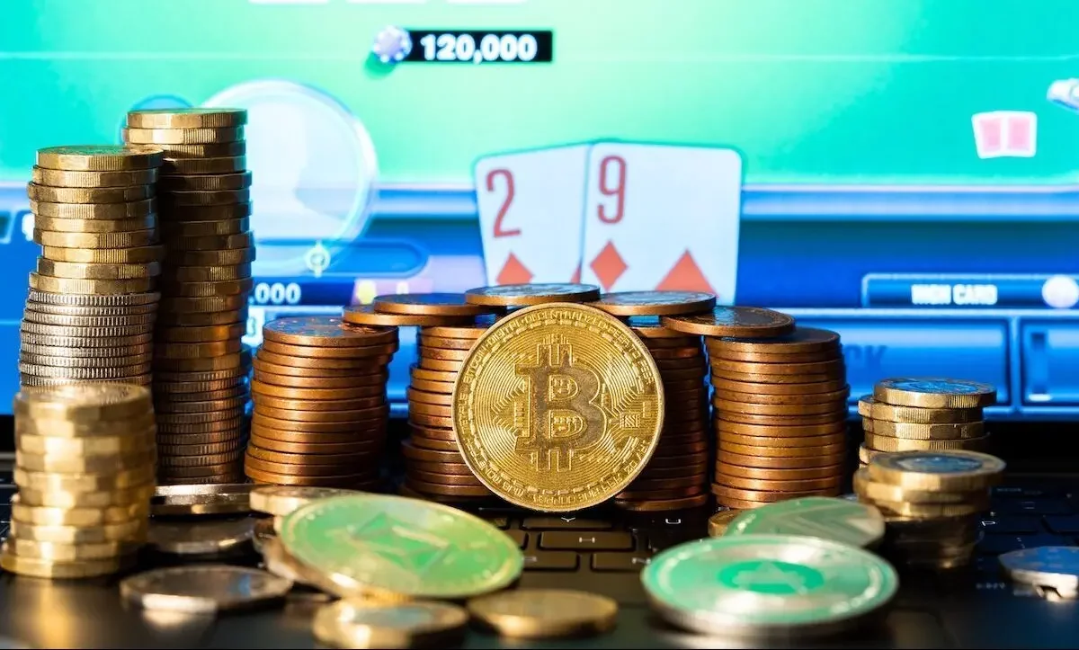 A bitcoin in front of a stack of coins and an online poker site