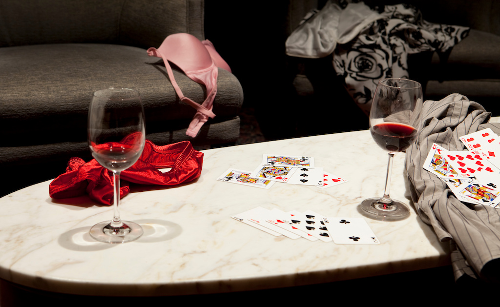 The outcome of a game of strip poker with women's clothing strewn over a chair and table and a man's shirt on the right side.Two partly full glasses of wine are also on the table.