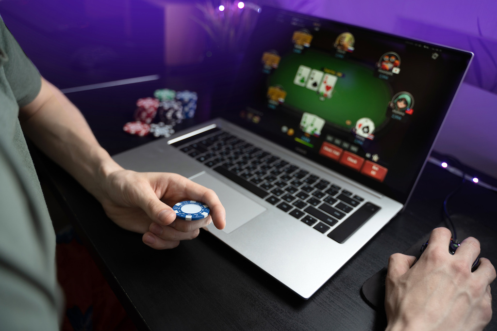 Young man play online poker in laptop. Unrecognizable person in neon light.