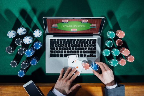 Man playing online poker with laptop on a green table with chips all around