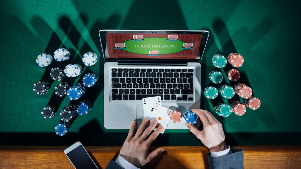 Man playing online poker with laptop on a green table with chips all around