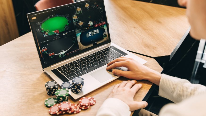 A person playing multiple tables of online poker next to a pile of poker chips.